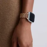 A person is wearing a smartwatch with a rose gold metal link bracelet on their wrist, against a background of brown fabric.
