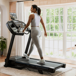 A person exercises on a Horizon treadmill positioned in a well-lit room with large windows.