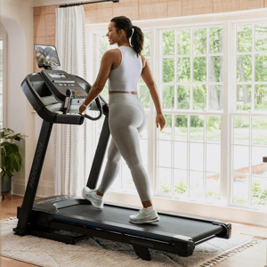 A person exercises on a Horizon treadmill positioned in a well-lit room with large windows.