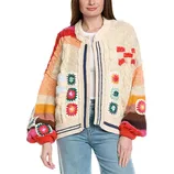A woman is wearing a colorful knitted sweater featuring a patchwork design with various patterns and colors, including red, blue, and orange accents. She pairs it with light blue jeans.