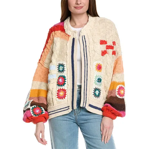 A woman is wearing a colorful knitted sweater featuring a patchwork design with various patterns and colors, including red, blue, and orange accents. She pairs it with light blue jeans.