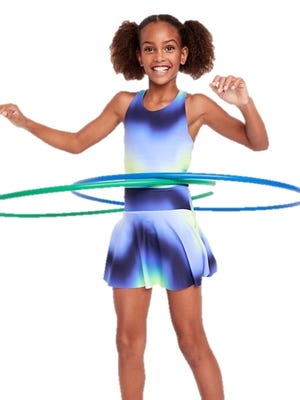 A smiling girl is using two hula hoops while wearing a blue and green gradient dress with a flared skirt.