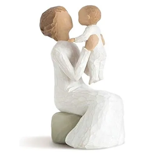 A carved figurine of a seated woman holding an infant, both dressed in white, with a focus on the simplicity and warmth of the parent-child relationship.