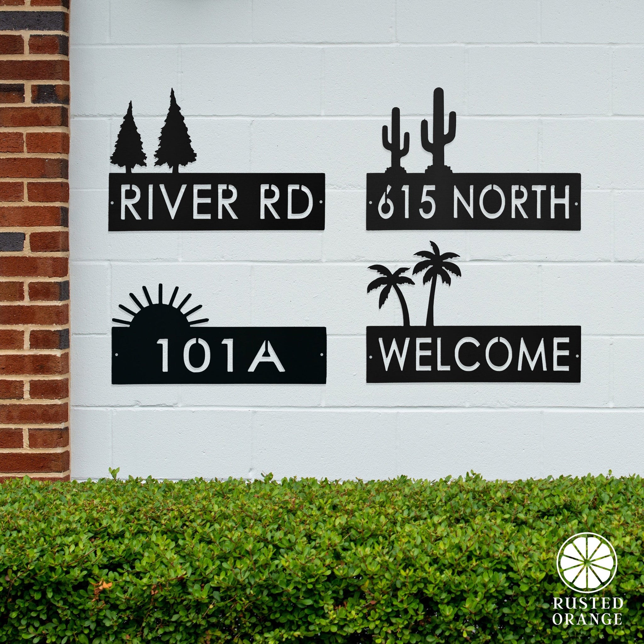 Metal wall signs with silhouettes: \“RIVER RD\“ with pine trees, \“615 NORTH\“ with cacti, \“101A\“ with a sun, and \“WELCOME\“ with palm trees.