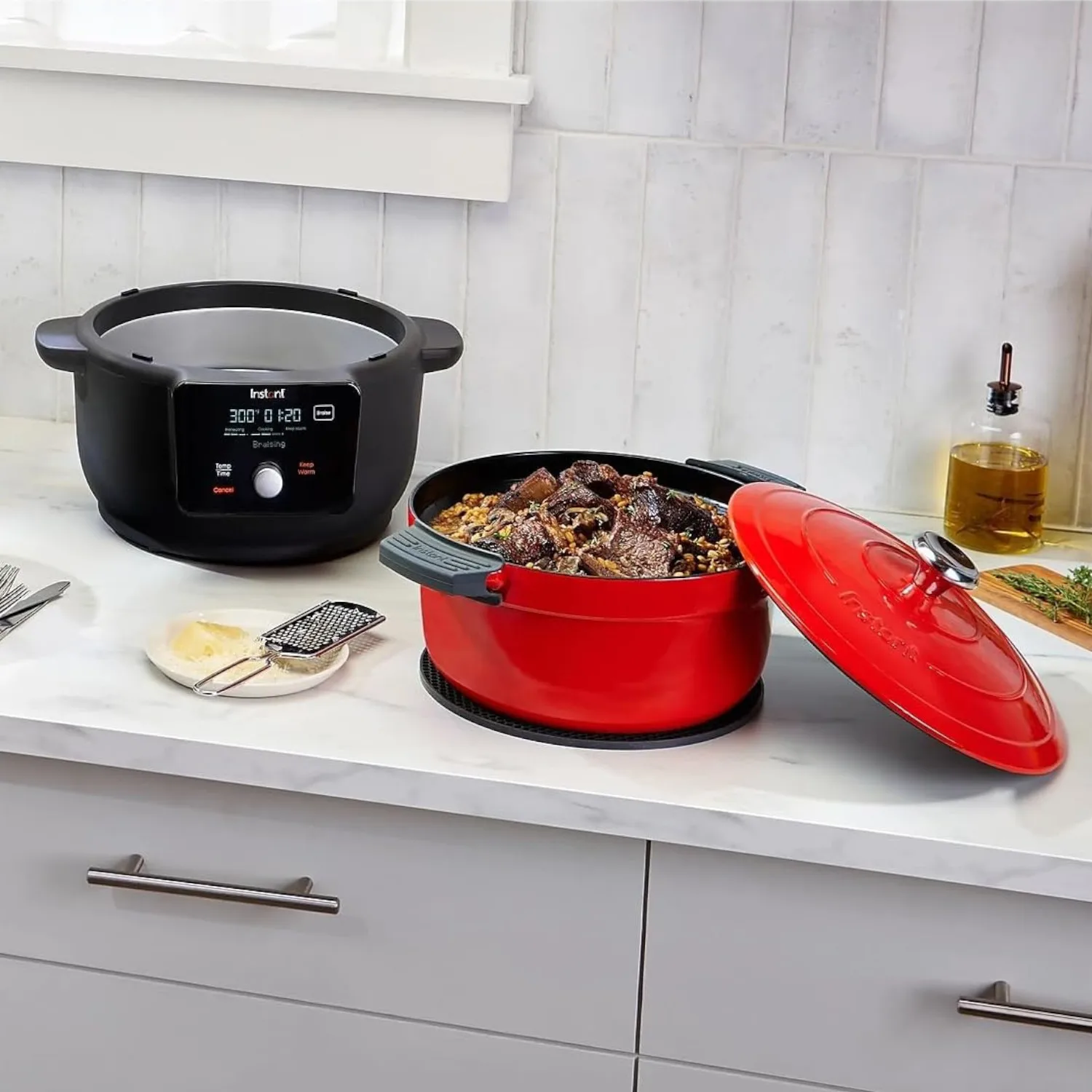 A black electric multi-cooker and a red enameled cast iron Dutch oven with a lid, containing food, on a kitchen counter.