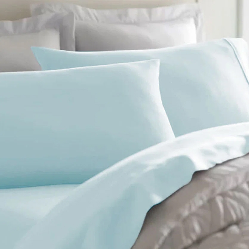 Light blue bed sheets and pillowcases are shown neatly placed on a bed with a gray quilt at the foot.