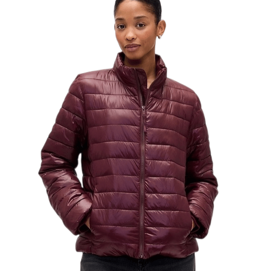 A woman is wearing a maroon quilted puffer jacket with a high collar and zipper closure, paired with dark jeans.