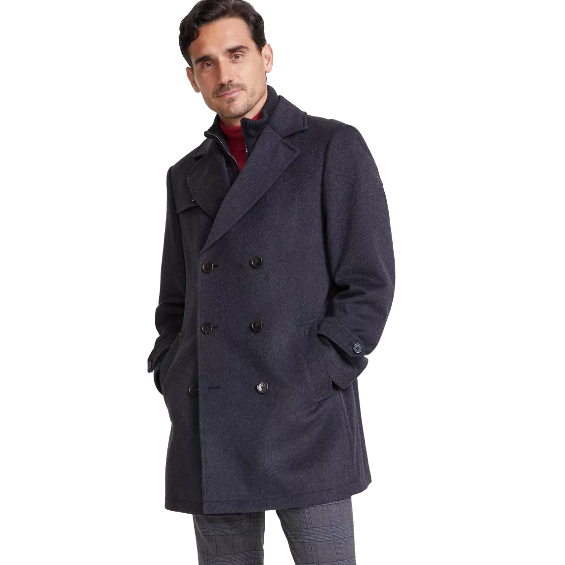 A man is wearing a dark gray double-breasted pea coat with black buttons, paired with a red turtleneck and plaid trousers.