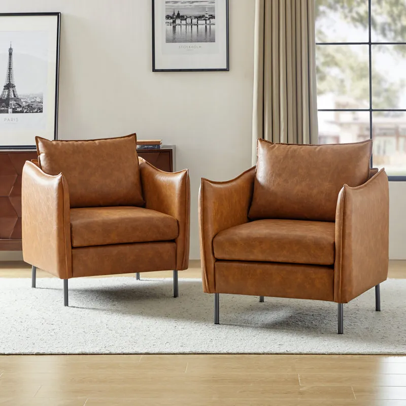 A pair of contemporary armchairs with brown faux leather upholstery and sleek metal legs, set in a modern living room with neutral decor, including framed art and large windows.