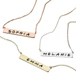 Three necklaces with rectangular pendants are shown, each engraved with a name: \“SOPHIA\“ on a rose gold chain, \“EMMA\“ on a gold chain, and \“MELANIE\“ on a silver chain.