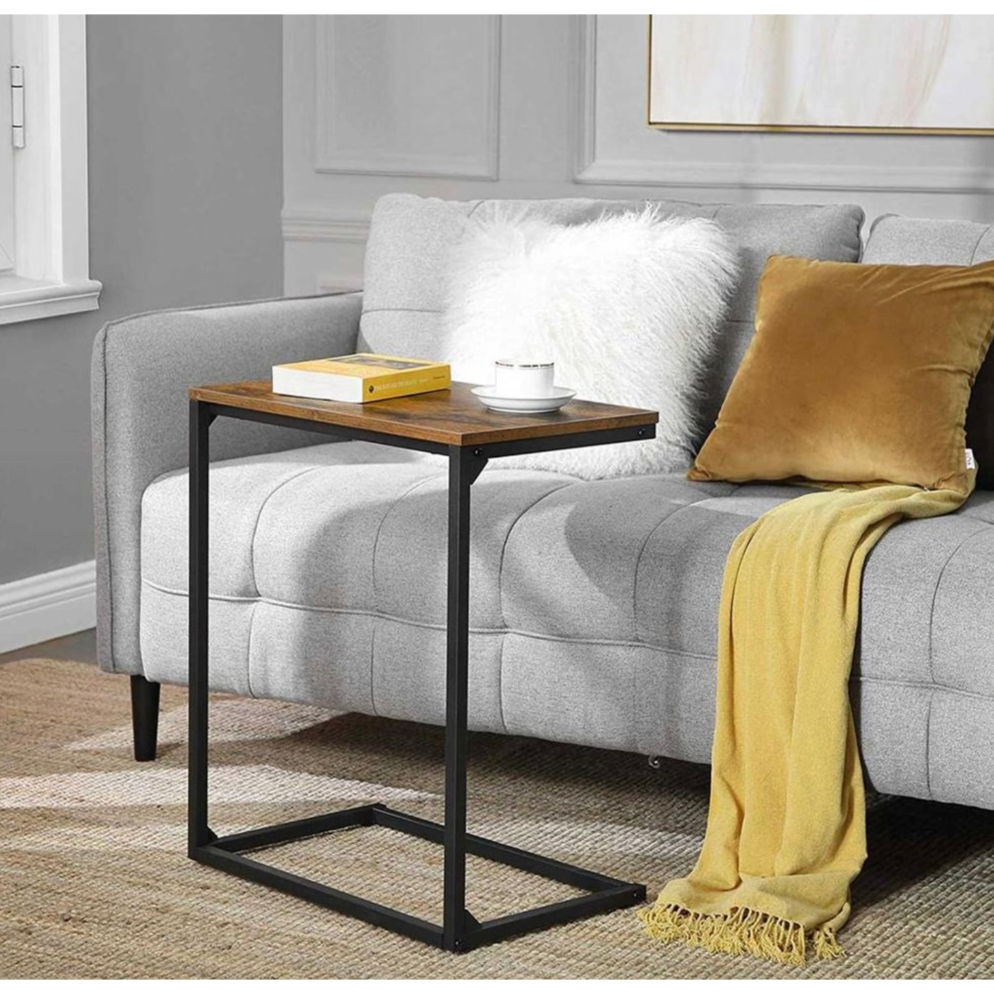 A C-shape end table with a wooden top and metal frame, positioned beside a gray sofa with white and mustard pillows.