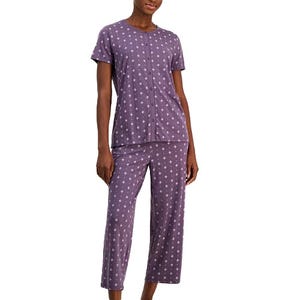 A woman is wearing a two-piece pajama set with a purple background and white star pattern, consisting of a short-sleeve top and capri-length pants.