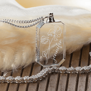 A rectangular crystal keychain with a chain, featuring engraved flowers and the name \“Jennifer\“ in cursive. It's displayed on a soft, furry surface and accompanied by a sparkling chain accessory.