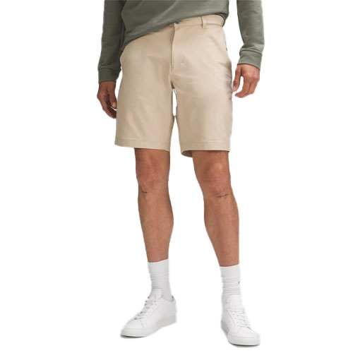 A person is wearing beige shorts paired with a green long-sleeve shirt and white sneakers with socks.