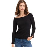 A woman models a black, off-the-shoulder ribbed sweater with long sleeves featuring slit cuffs. She pairs it with blue jeans and gold hoop earrings.