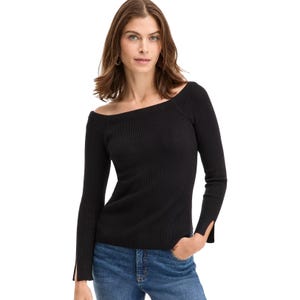 A woman models a black, off-the-shoulder ribbed sweater with long sleeves featuring slit cuffs. She pairs it with blue jeans and gold hoop earrings.