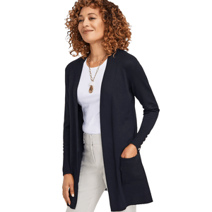 A person wears a navy open-front cardigan with button details on the sleeves, paired with a white shirt, beige pants, and a long necklace.