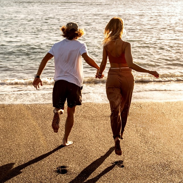 A couple is running hand in hand towards the ocean on a sandy beach.