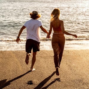 A couple is running hand in hand towards the ocean on a sandy beach.