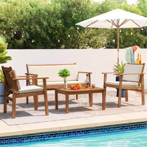 4-piece patio set includes a sofa, two armchairs, and a coffee table, all made of acacia wood with white cushions. It is set by a poolside with an umbrella, plants, and outdoor decor like string lights.