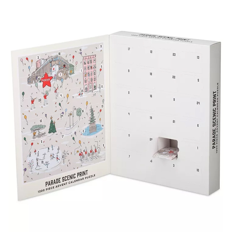 Macy's Parade Puzzle Advent Calendar features a 1200-piece puzzle with a scenic print, revealing pieces behind numbered slots. The calendar showcases festive imagery like balloons, Christmas trees, and ice skaters, offering a new puzzle piece each day.