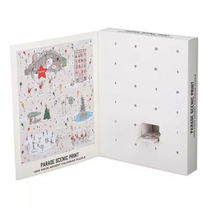 Macy's Parade Puzzle Advent Calendar features a 1200-piece puzzle with a scenic print, revealing pieces behind numbered slots. The calendar showcases festive imagery like balloons, Christmas trees, and ice skaters, offering a new puzzle piece each day.