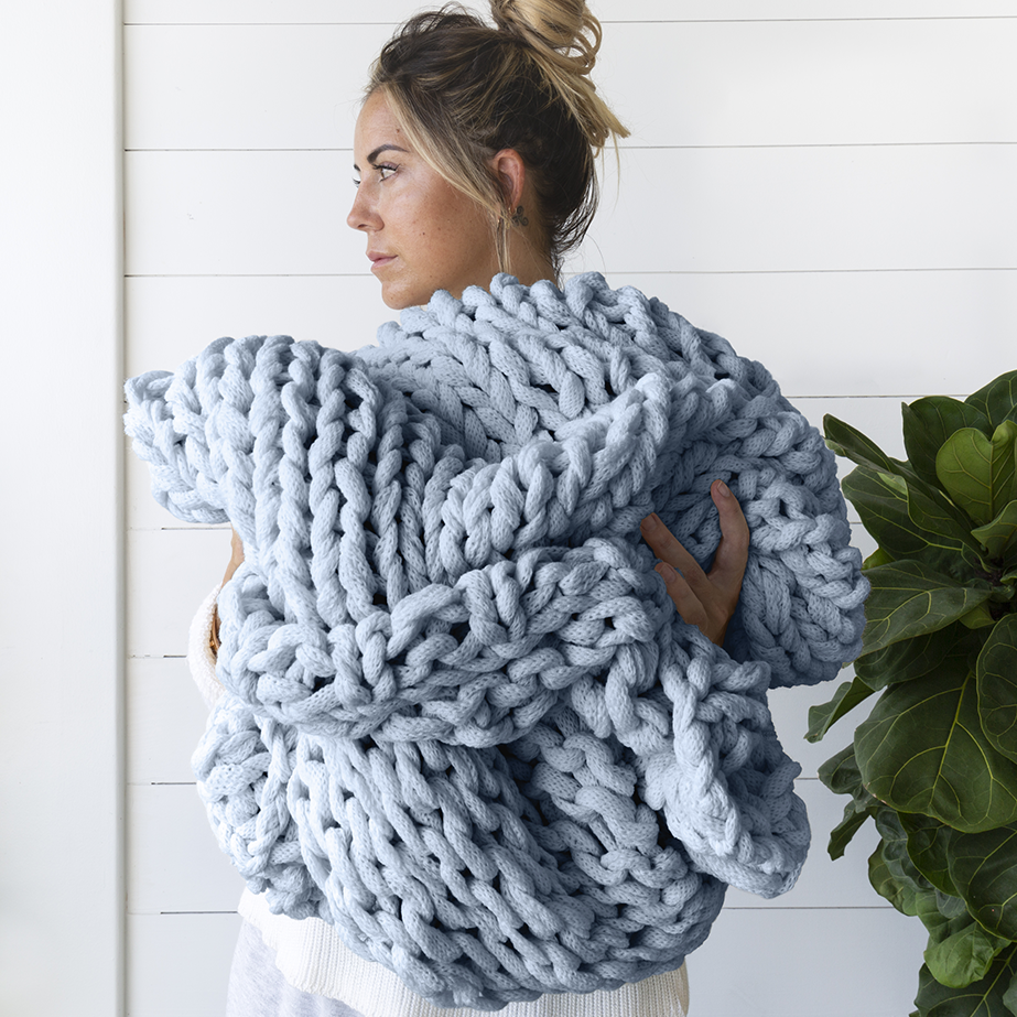 A woman is wrapped in a chunky, oversized light blue knit blanket.