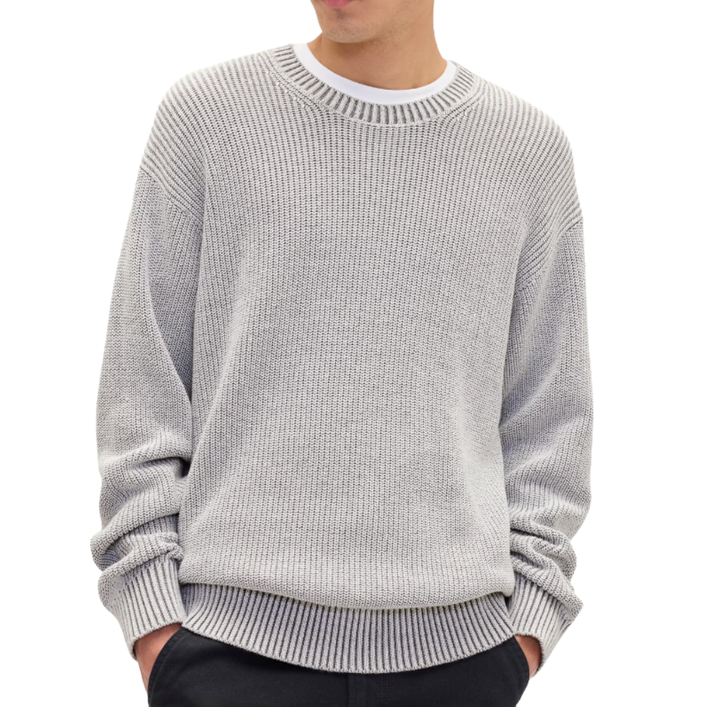 A person is wearing a light gray knit sweater with a ribbed design, layered over a white shirt, and paired with dark pants.