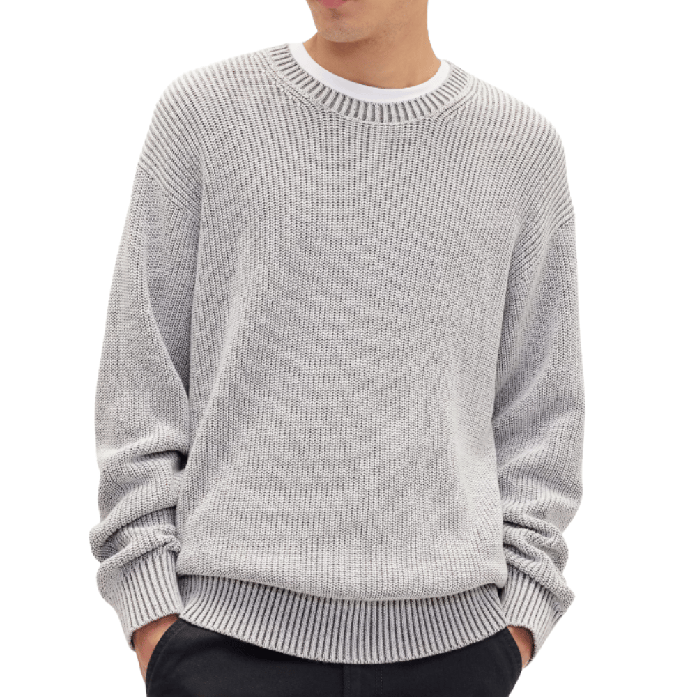 A person is wearing a light gray knit sweater with a ribbed design, layered over a white shirt, and paired with dark pants.