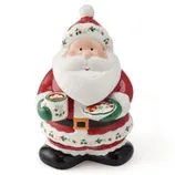 A Santa-themed ceramic cookie jar, featuring Santa Claus holding a mug and a plate, decorated with festive holly accents.