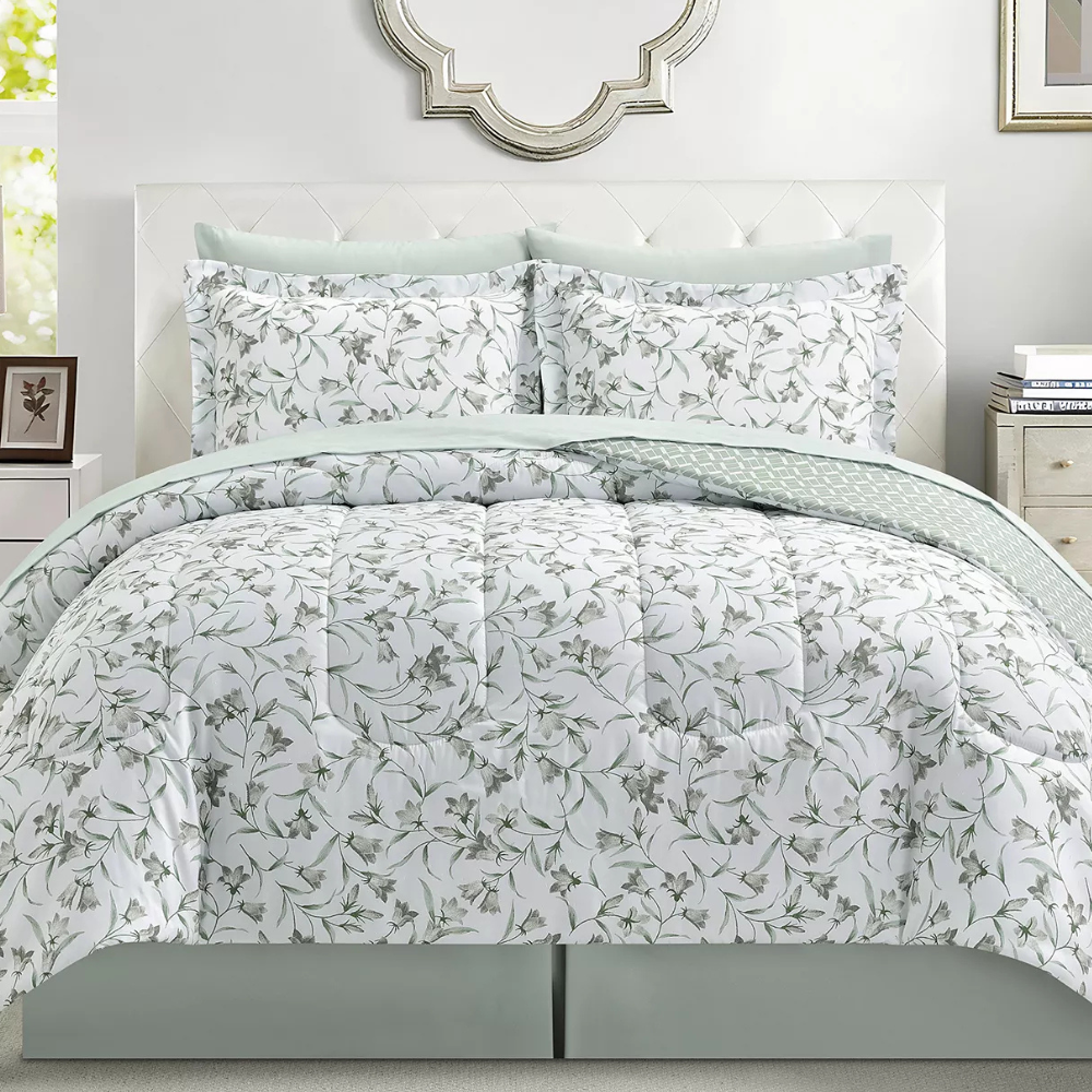 A bed is adorned with a floral-patterned comforter set, including matching pillow shams. The bedding features a white background with green leafy designs, complemented by light green accents.