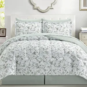 A bed is adorned with a floral-patterned comforter set, including matching pillow shams. The bedding features a white background with green leafy designs, complemented by light green accents.