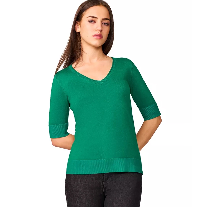 A woman is wearing a green V-neck knit top with elbow-length sleeves and dark jeans.