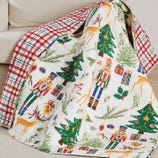 Reversible holiday-themed quilt with a Nutcracker, Christmas trees, reindeer, gifts, and holly pattern on one side, and a red and white checkered design on the other.