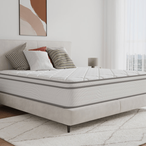 A 14-inch hybrid queen mattress with a quilted top, featuring a white and gray design. It rests on a light upholstered bed frame with a neutral-toned, modern bedroom setting, including decorative pillows and a patterned area rug.