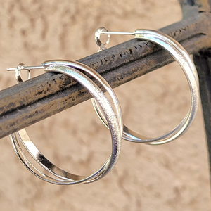 Silver hoop earrings with a polished and textured design hanging on a rustic metal rod.