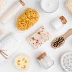Assorted bath and body care items including soaps, loofah, sea sponges, a hairbrush, bath salts, a candle, and a massage tool.