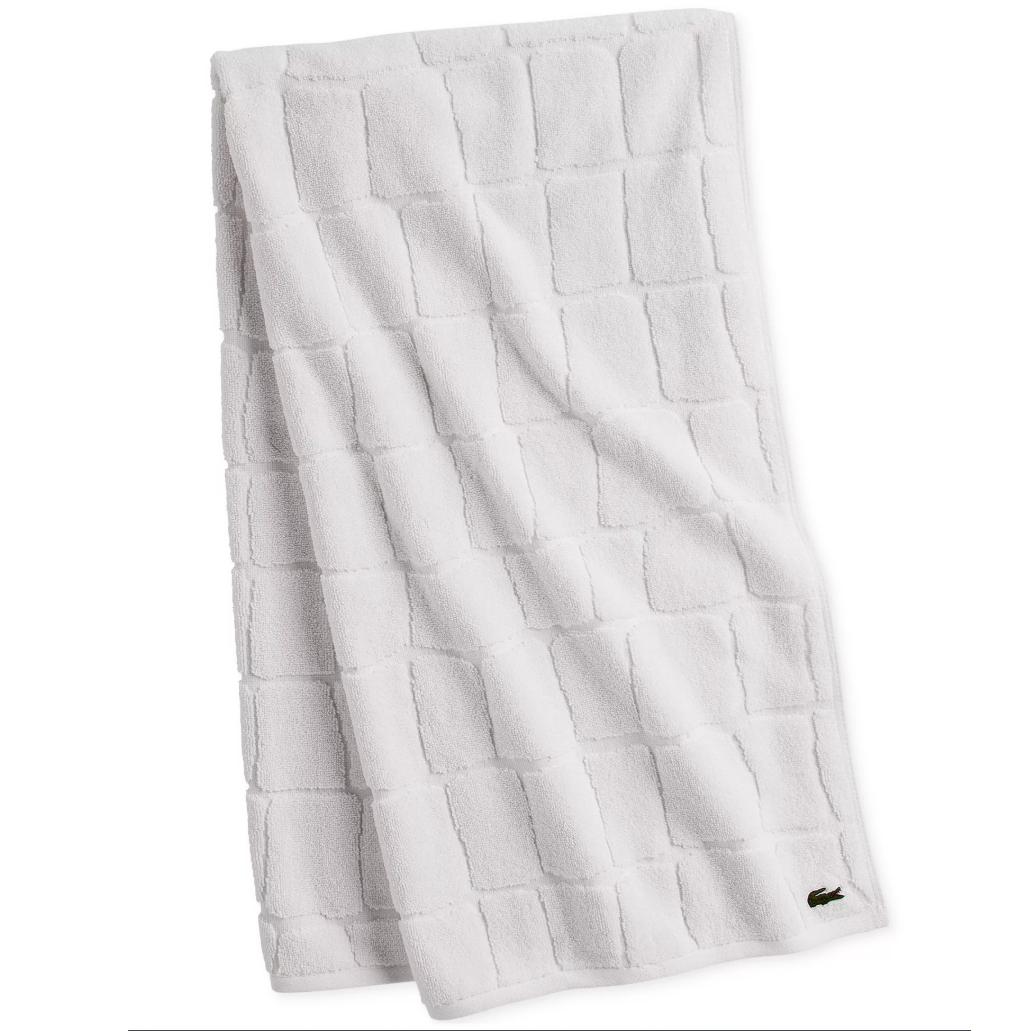 White towel with a textured square pattern and a small embroidered logo of a crocodile in the corner.