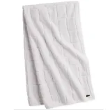 White towel with a textured square pattern and a small embroidered logo of a crocodile in the corner.