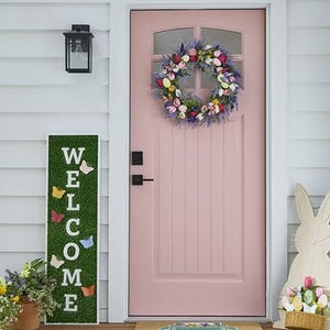 A green vertical porch sign with white letters spelling \“WELCOME,\“ decorated with colorful butterfly silhouettes.