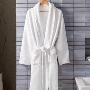 A white, plush cotton spa robe with a shawl collar, waist tie, and two front pockets, hanging on a wooden hanger against a tiled background.