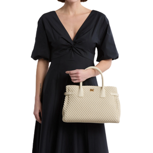 A person in a black dress holds a beige textured handbag with short handles.