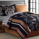 Black and gold comforter with ornate patterns, brown bedskirt, and complementary pillows in a bedroom setting.