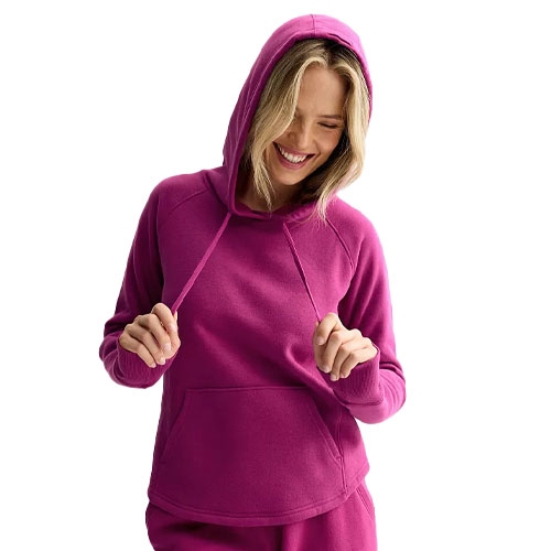 A person is wearing a bright pink hoodie with a kangaroo pocket and matching sweatpants, smiling and holding the hood drawstrings.