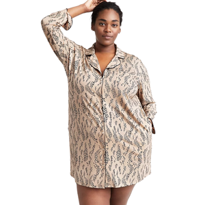 A person is wearing a long-sleeve, button-up pajama shirt featuring a beige base with a black abstract pattern. The shirt has a relaxed fit and includes a front pocket.