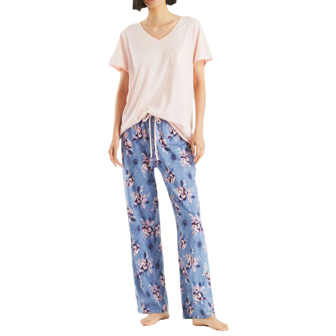 A woman is wearing a pajama set with a light pink V-neck short-sleeve top and blue drawstring pants featuring a floral print.