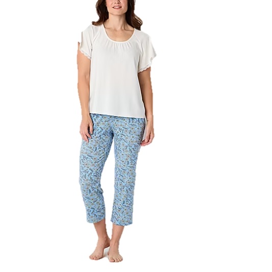 A woman is wearing a white short-sleeve top with a scoop neckline and blue floral-patterned cropped pants, standing barefoot.