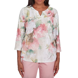 Alfred Dunner Printed Roses Top features a floral pattern with pink, green, and white tones on a textured fabric. It has three-quarter sleeves and a keyhole neckline detail, paired here with light pink pants.