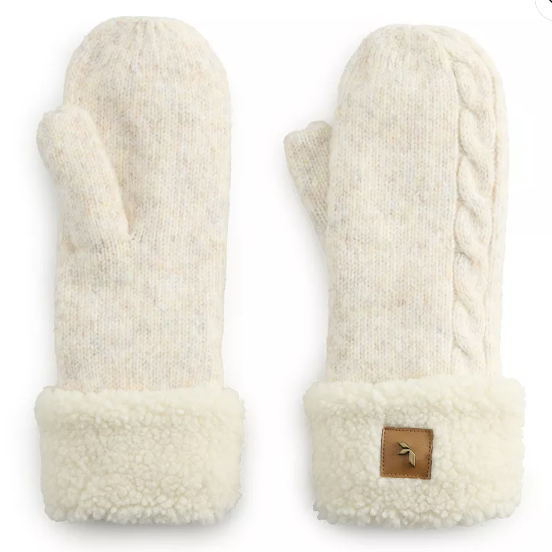 Cream-colored knit mittens with a cable knit design on one side and plush fleece cuffs featuring a small leather patch.