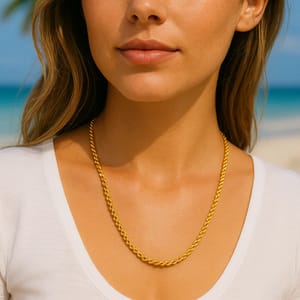 A gold rope chain necklace is worn by a person in a white shirt, set against a beach background.